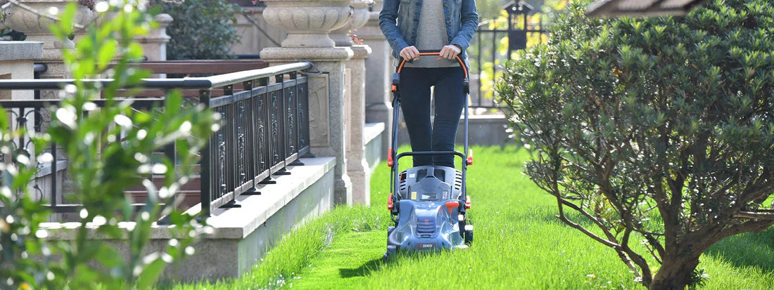 Person mowing green lawn with push lawn mower near garden fence and shrubs on sunny day