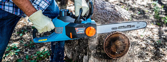 Man wearing gloves using blue Senix electric chainsaw to cut tree log outdoors