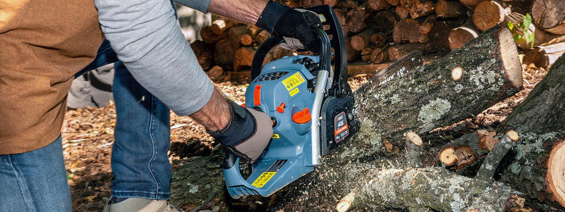 Person wearing gloves starting blue gas chainsaw to cut tree logs outdoors with woodpile in background
